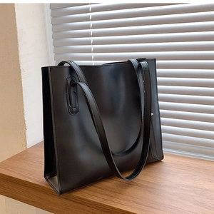 Detail of black leather tote bag featuring modern metal eyelets and long shoulder straps
