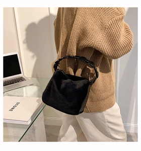 Detail of black faux fur bucket bag featuring leather handle and gold chain strap