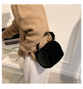 Detail view of black faux fur cylinder bag with leather handle and gold chain strap