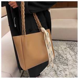 Détail du sac fourre-tout chameau avec poignée tressée et ruban décoratif sur la sangle