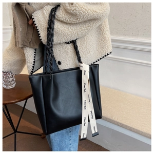 Détail d'un cabas en cuir noir avec poignées tressées et ruban décoratif chic