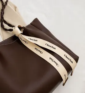 Détail d'un cabas en cuir marron avec surpiqûres blanches et une sangle tissée logo