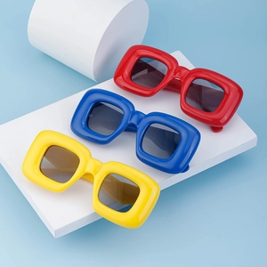Three pairs of thick square frame sunglasses in red, blue, and yellow on a white platform