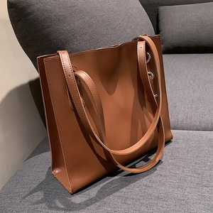 Classic large brown leather tote bag for women with metallic strap rings on a sofa