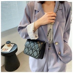 Model wearing black quilted crossbody bag with metal chain strap on a purple suit