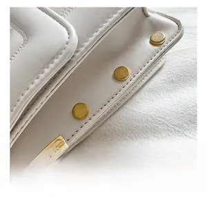 Detailed macro view of gold rivets and precise stitching on white leather crossbody bag