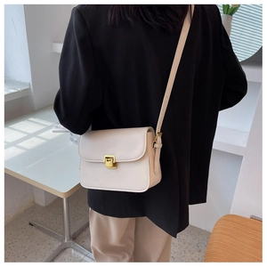 Détail d'un sac bandoulière beige avec boucle dorée porté sur un blazer noir