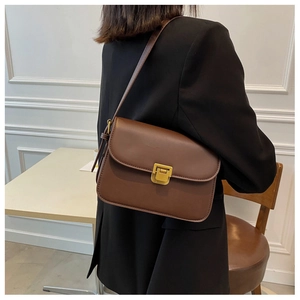Détail d'un sac à bandoulière en cuir marron avec fermoir doré sur une veste noire