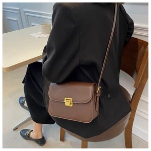 Détail d'un sac bandoulière en cuir marron avec boucle dorée sur un blazer noir classique