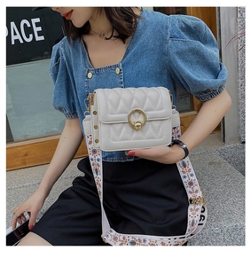 Detail of white quilted crossbody bag with gold round buckle and ethnic embroidered strap