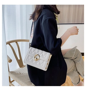 Close-up of white quilted crossbody bag with gold round lock and embroidered wide strap