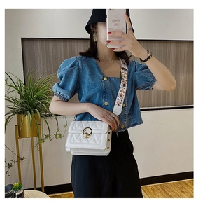 Close-up of white quilted crossbody bag with gold ring clasp and ethnic embroidery strap