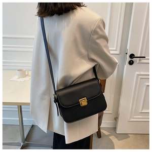 Détail d'un sac bandoulière en cuir noir mat avec fermoir doré porté par un mannequin