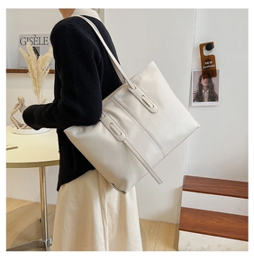 Detail of a minimalist cream tote bag with vertical strap accents shown on a model