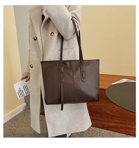 Side view of large dark brown leather tote bag worn by model in a stylish wool coat