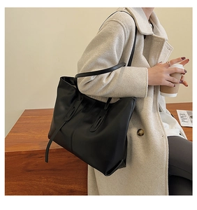 Detail of a large black leather tote bag worn by a model in a cozy winter setting