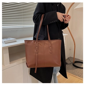 Brown leather tote bag detail with vertical stitching on model in a minimalist room