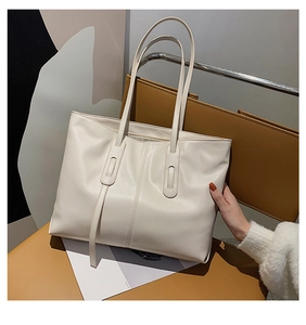 Detail of a large cream tote bag with vertical stitching on a brown leather chair