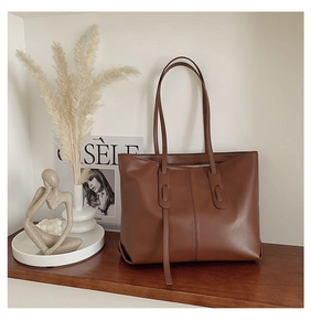 Brown leather tote bag on wooden shelf with abstract decor in a cozy home setting
