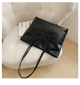 Detail of a large black leather tote bag featuring parallel stitching on a soft sofa