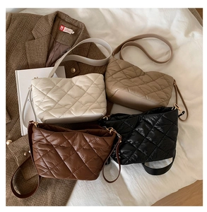 Quilted crossbody bucket bags in four warm colors displayed on a minimalist bedding