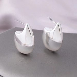 Polished silver teardrop stud earrings with a minimalist C-shape on a satin background