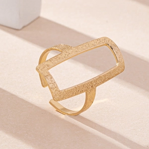 Anello aperto quadrato dorato con texture sabbiata opaca su base beige moderna