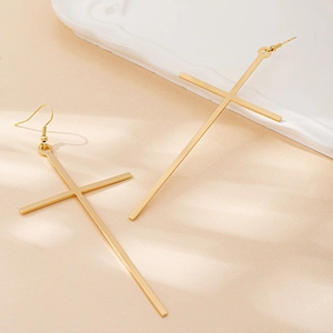 Minimalist long gold cross earrings with hook and stud closure on a ceramic tray