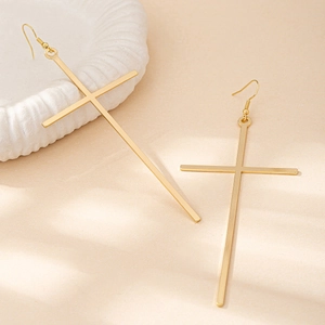 Minimalist long gold cross drop earrings with fishhook wires on a white ceramic plate