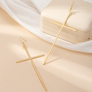 Detail of large gold cross drop earrings with hooks displayed on elegant silk background