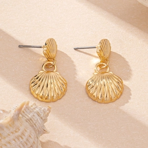 Detailed view of gold scallop shell earrings on sand background with a conch shell