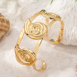 Macro view of gold seashell spiral cuff bracelet on sand with white coral and shells