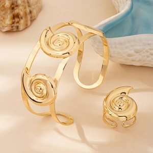 Detail of gold spiral shell bangle and ring set with ocean-themed props and seashell