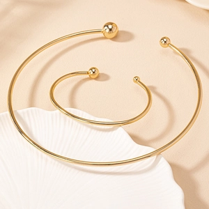 Polished gold geometric choker and matching bracelet set with spherical ends on white tray