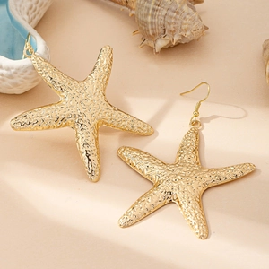 Golden starfish dangle earrings with hammered texture on a beach sand background