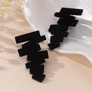 Fashionable black matte acrylic geometric staircase earrings on beige textured background