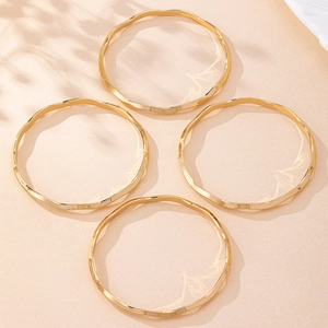 Detailed view of four wavy gold bangles arranged on a minimalist beige surface