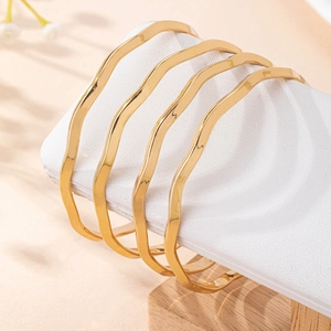 Set of four minimalist gold wavy bracelets with a polished finish on white leather