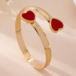 Detail of gold-plated open bangle with red enamel heart charms on a soft background