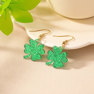 Close-up of green shamrock earrings with glitter resin and golden hooks on white tray