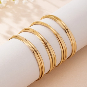 Minimalist gold geometric stackable bangles set displayed on a white leather prop