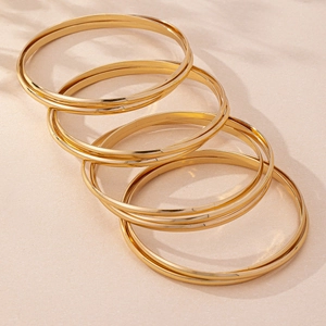 Detail of four-piece minimalist gold geometric bangles with a polished finish and shadows