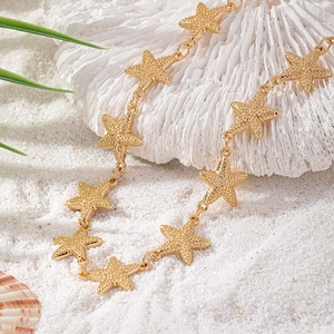 Detail of golden starfish necklace with relief texture on white coral and sand