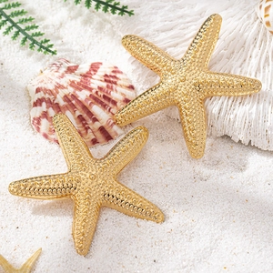 Golden starfish stud earrings with embossed texture on white beach sand with seashells