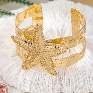 Golden starfish open cuff bracelet with hammered texture on a coral-like display base