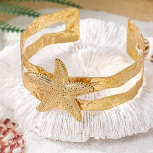 Detailed view of golden starfish cuff bracelet on white coral with beach sand texture