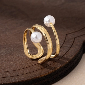 Close-up of golden spiral ring with dual white pearls on a minimalist wood surface
