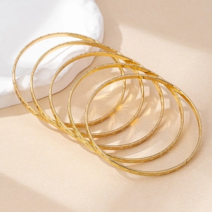 Detail of five stackable gold bangles with vintage engraved textures on a ceramic plate