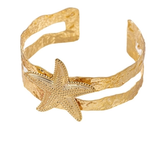 Golden starfish cuff bracelet with textured hammered wave band on white background