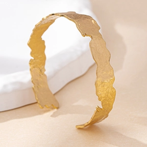 Detailed close-up of golden cuff bracelet with hand-hammered texture and organic finish